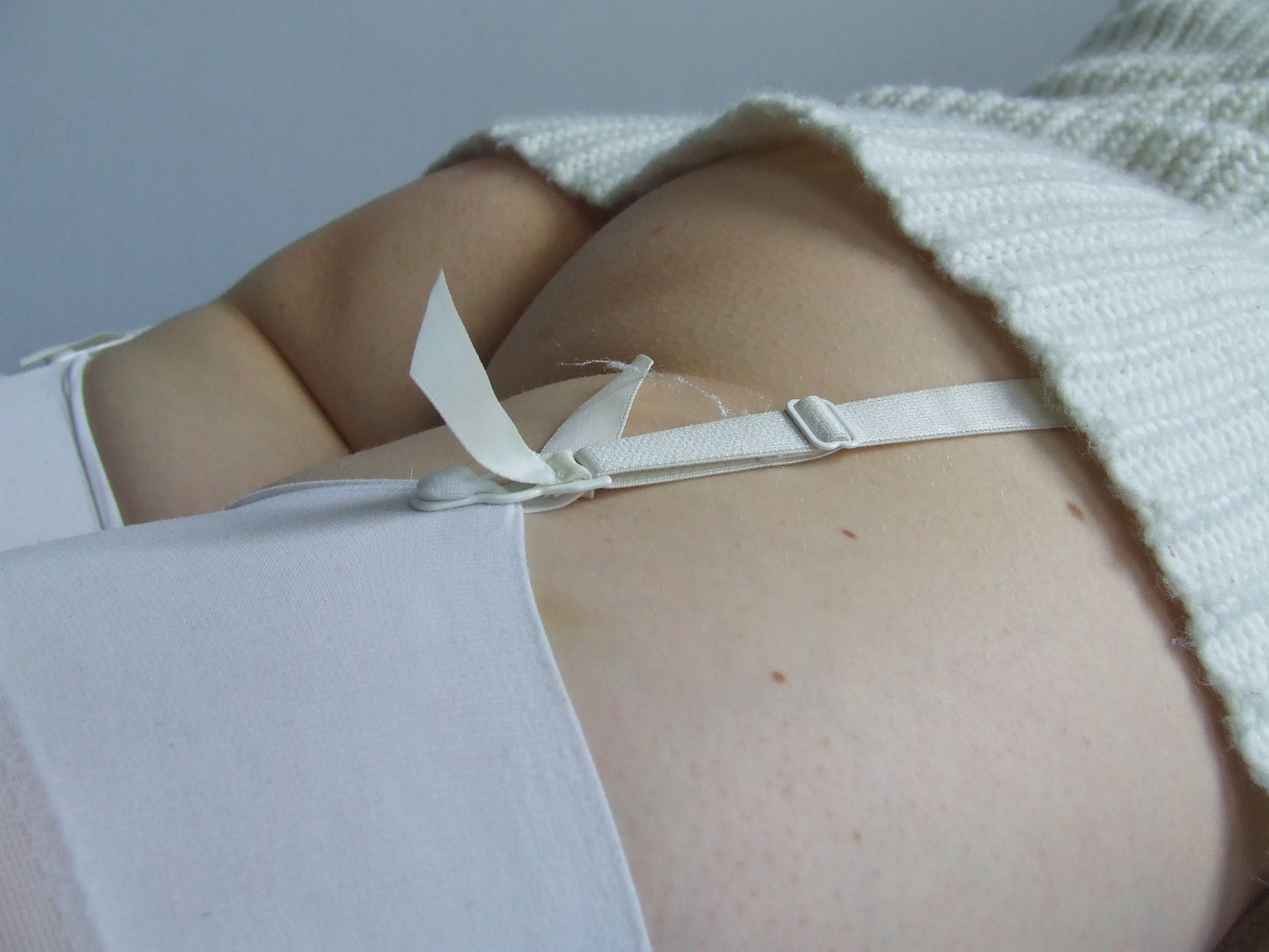 Shizuka Kawa lying down flat on a bed on her belly, dressed in beige sweater and white lace-trimmed stockings. Focus on garter straps. Zoomed in on the butt.