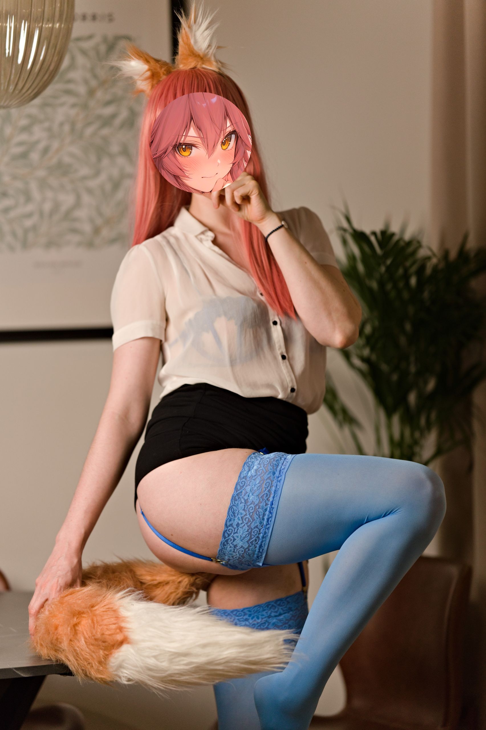 Shizuka Kawa cosplaying as Tamamo-no-Mae from Fate/Grand Order dressed in a sheer white button-down shirt, black miniskirt, and blue lace lingerie with blue stockings. She stands against a table with her leg curled up, showing her blue lace-trimmed stockings attached by a grater straps. A large white-tipped fox tail rests on the table.