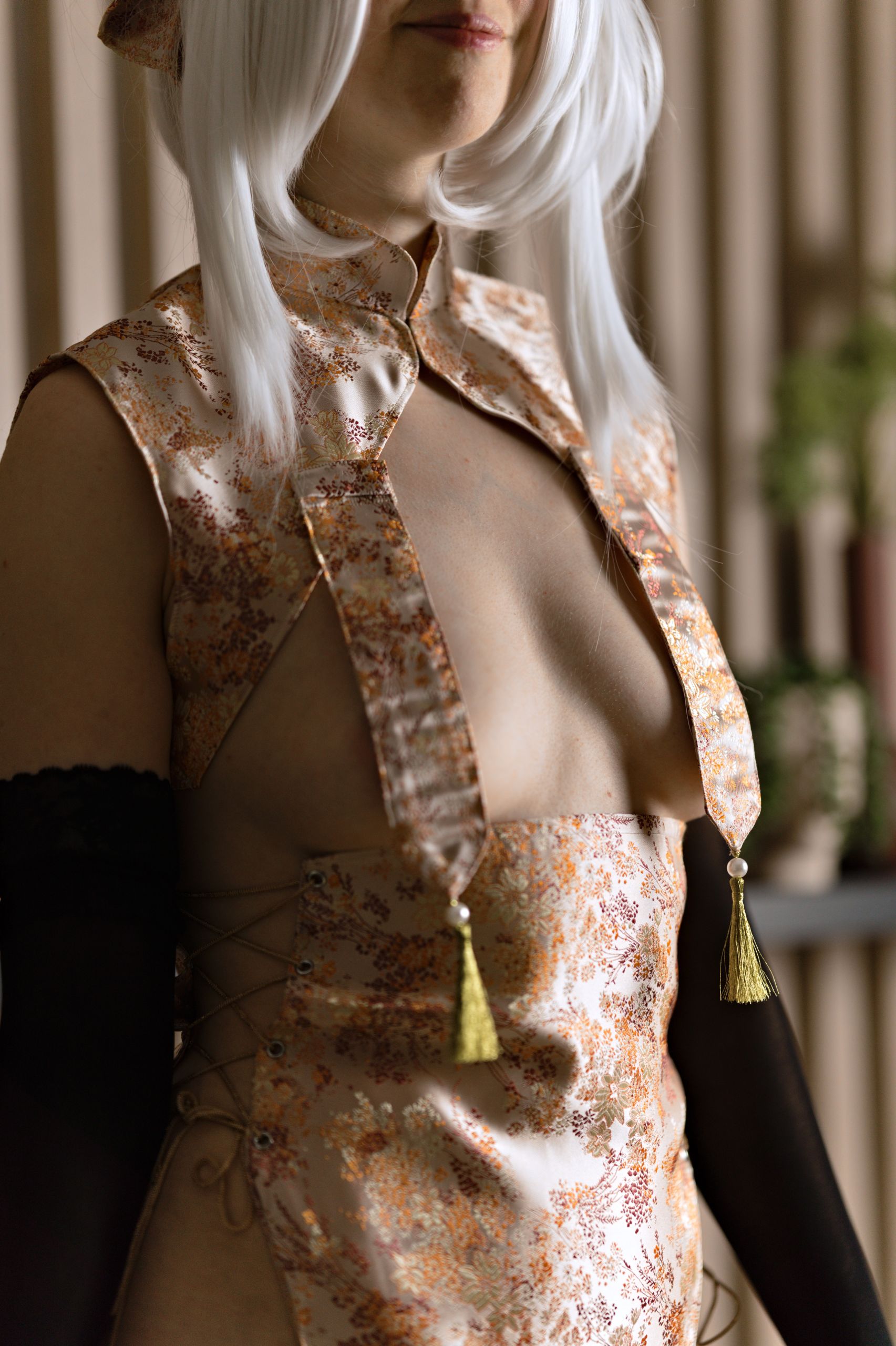 Shizuka Kawa cosplaying as Sirius from Azur Lane dressed in a silk qipao with boobie flaps ending in gold tassels. She stands facing forward with her chest pushed out, highlighting her bare skin and cleavage.